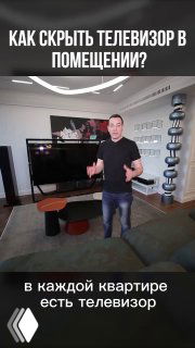 Фото интерьера: гостиная с крупным телевизором на фоне большой тёмной картины-подложки; мужчина-дизайнер стоит у экрана.