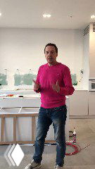 Дизайнер в розовом свитере демонстрирует кухонный остров с деревянным слэбом и инструментами, виден монтаж парящей столешницы.