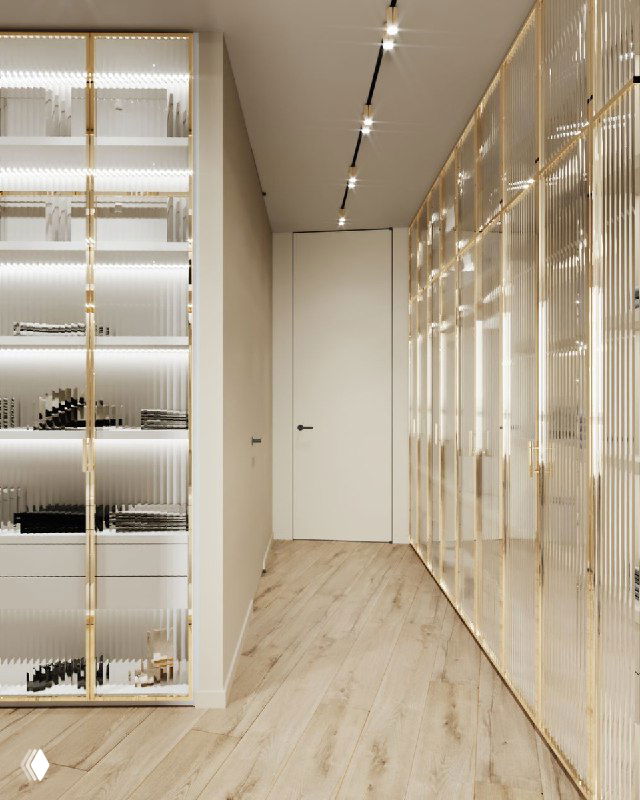 Узкий проход гардеробной с напольным покрытием светлого дерева и встроенными шкафами с глянцевыми фасадами и подсветкой для удобства хранения.