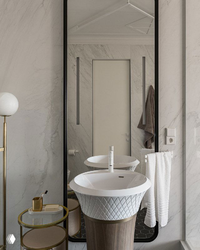 Белая отдельно стоящая раковина Falpe на круглой деревянной тумбе, высокое прямоугольное зеркало и мраморные стены в оформленной ванной комнате.