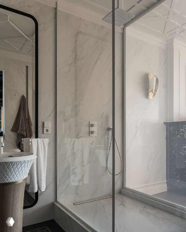 Прозрачная стеклянная перегородка душевой с крупной потолочной лейкой, мраморная облицовка и проникновение солнечного света в пространство ванной.