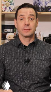 Портрет мужчины в рубашке на фоне образцов материалов и полок; кадр из видеообзора дизайн‑проекта квартиры с концепцией джунглей в городском интерьере.