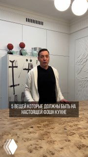 Мужчина в интерьере фэшн-кухни на фоне барельефа и встроенных панелей; видна столешница, декоративные детали.