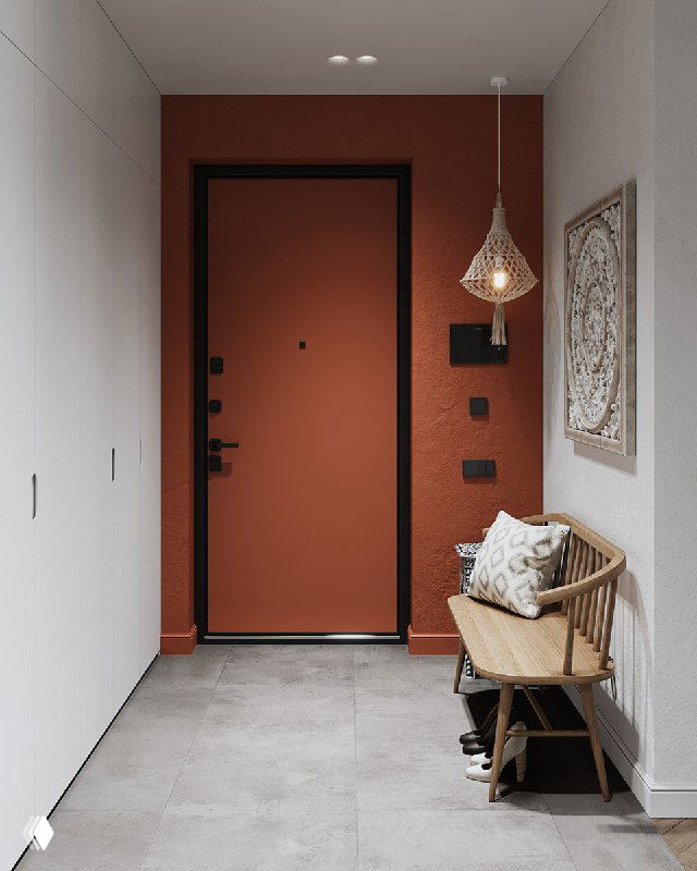 Прихожая с акцентной терракотовой стеной и входной дверью; вид с прохода, справа длинный белый шкаф, слева скамейка и декор у стены.