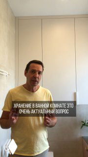 Мужчина стоит в ванной на фоне высокой плиточной стены и встроенных неглубоких шкафчиков; демонстрация идеи хранения и скрытия коммуникаций для порядка.