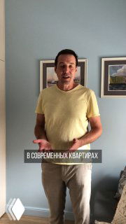 Человек стоит в гостевой комнате на фоне голубой стены и двух картин; интерьер показывает масштаб помещения и идею скрытого хозяйственного блока для стиральной машины.