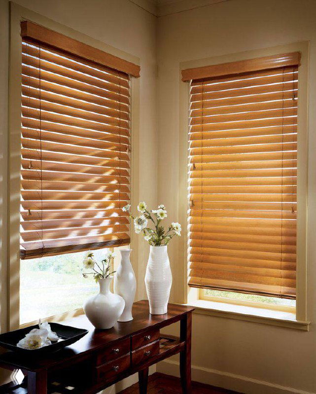Деревянные горизонтальные жалюзи на двух узких окнах в уютном уголке с консольным столиком и вазами, тёплый дневной свет.