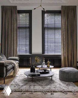 Комбинация штор и чёрных жалюзи в уютной гостиной с ковром и низким столом, мягкое рассеянное освещение создаёт атмосферу.