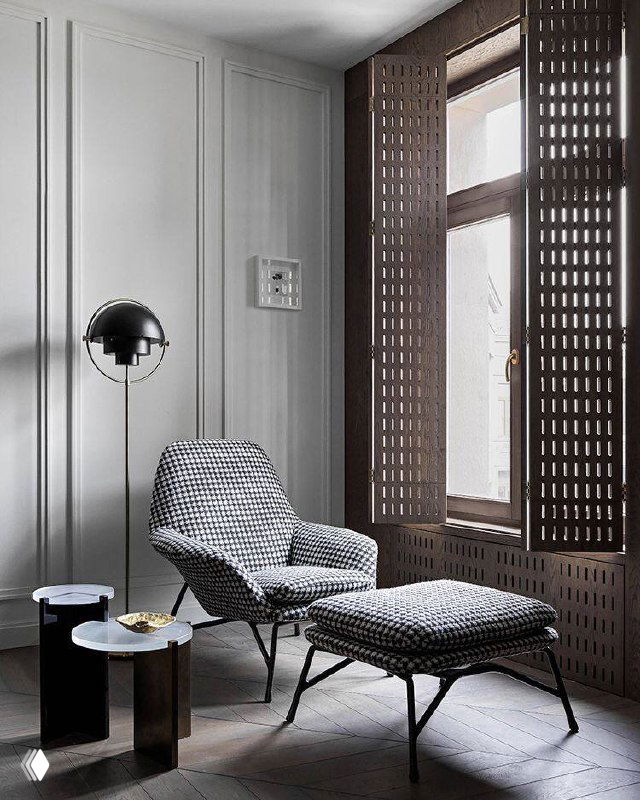 Сдержанный серый интерьер с перфорированными деревянными ставнями, креслом для отдыха и минималистичной приставной мебелью у окна.