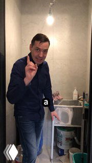 Демонстрация лайфхака в ванной: мужчина показывает раковину и ведро с отверстием для гофры, рядом строительные материалы.