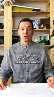 Дизайнер у стола с чертежом на фоне деревянных полок, объясняет решение: диагональная перегородка для шкафа в прихожей.