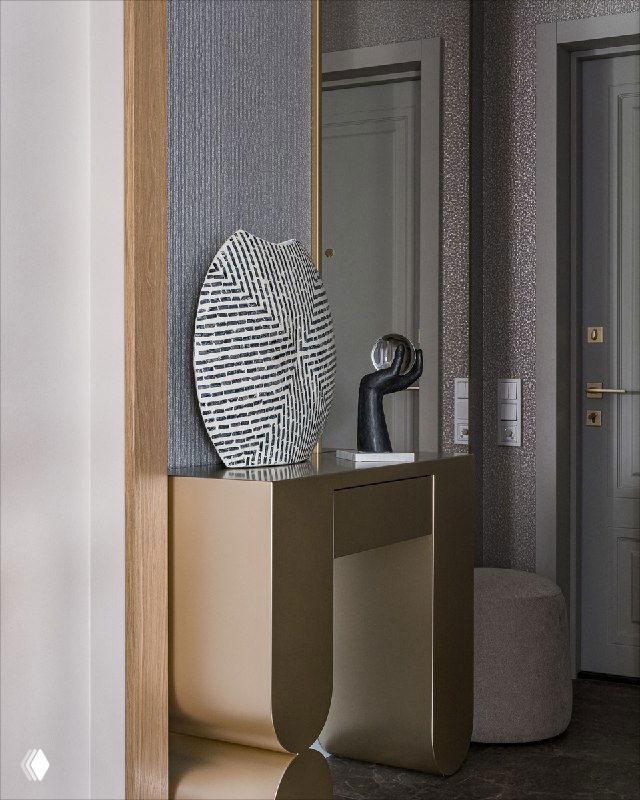 Фрагмент прихожей: бежево‑золотистая консоль, большое настенное зеркало и декоративный объект на столике; текстурная отделка стены и сдержанная палитра материалов.