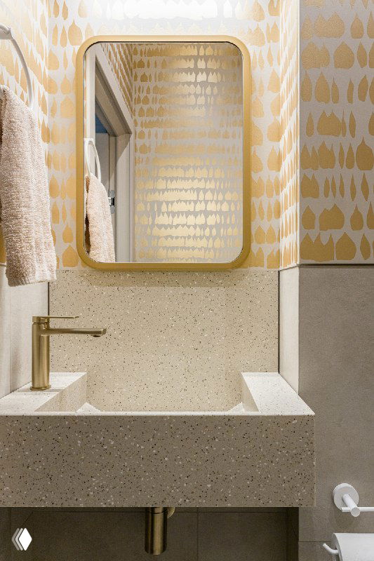 Миниатюрная раковина из искусственного камня по заказу, золотая смесительная арматура и зеркало в золотой раме на фоне художественного узора стен.