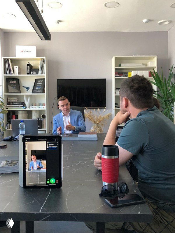 Практическая встреча: мужчина ведёт обсуждение за столом, смартфон снимает экран, вокруг участники обсуждают материалы и примеры решений для интерьера.