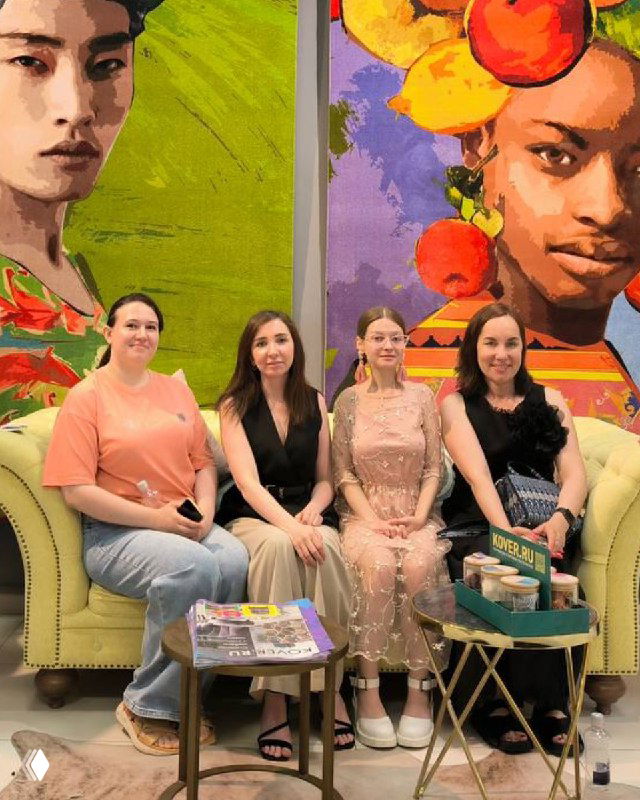 Группа участниц на красочном фоне: несколько женщин сидят на диване у стены с яркими художественными панно, уютная зона для обсуждений и визуальных примеров.