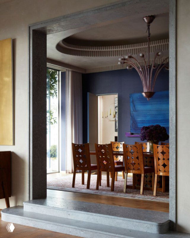 Интерьер столовой, вид через дверной проём с откосом из камня; ступени и обеденная зона, естественный свет и декор.