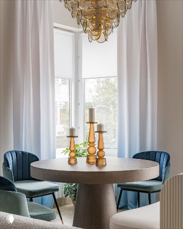 Обеденная зона с круглым столом, овальным островом и встроенным диваном, шторы с градиентом и крупная люстра Chloe.
