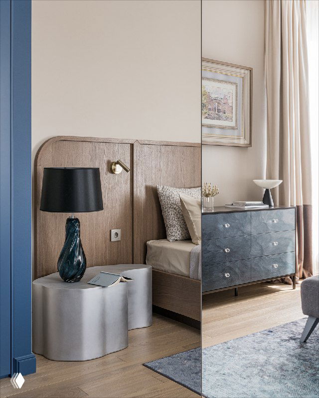 Спальня с зеркальными раздвижными дверями шкафа, отражающими прикроватную тумбочку и лампу, нейтральная палитра и текстуры.