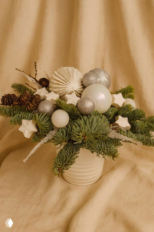 Низкая ваза с новогодней композицией из еловых веток, шишек и белых шаров на мягком бежевом фоне