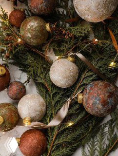 Фактурные шаровые ёлочные игрушки в тёплых коричневых и золотых тонах на хвое с гирляндой — идея сезонного декора и текстурных покрытий.