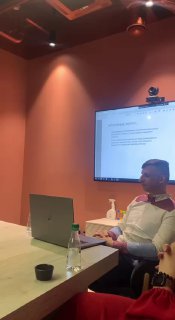 Спикер сидит за столом с ноутбуком, на стене экран с презентацией — рабочий формат разбора и консультации по кейсам.