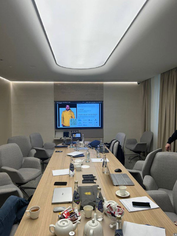 Переговорная перед презентацией: длинный стол с ноутбуками и чашками, экран с слайдом и подготовленные материалы для выступления.