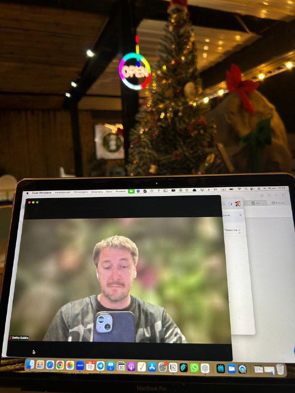 Ноутбук с открытой видеоконференцией в кафе на фоне праздничной ёлки — сочетание удалённой работы и отдыха в поездке.