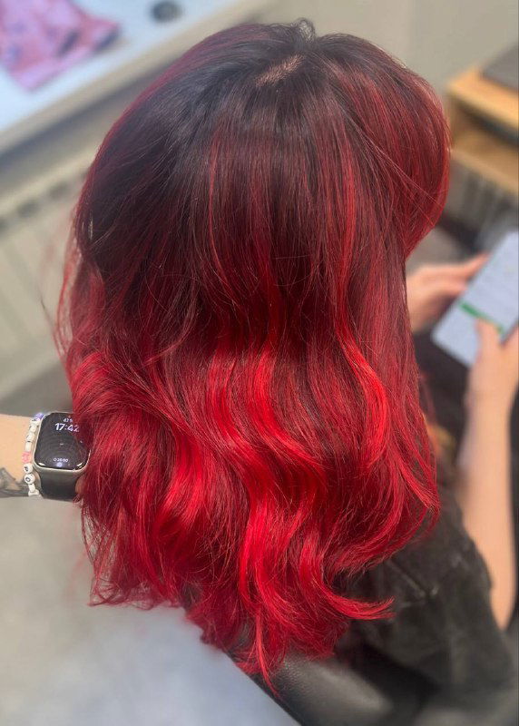 Глянцевые волнистые волосы с интенсивными красными прядями у лица, фото в салонной обстановке HairPositive, вид со спины‑сбоку, выраженный блеск.
