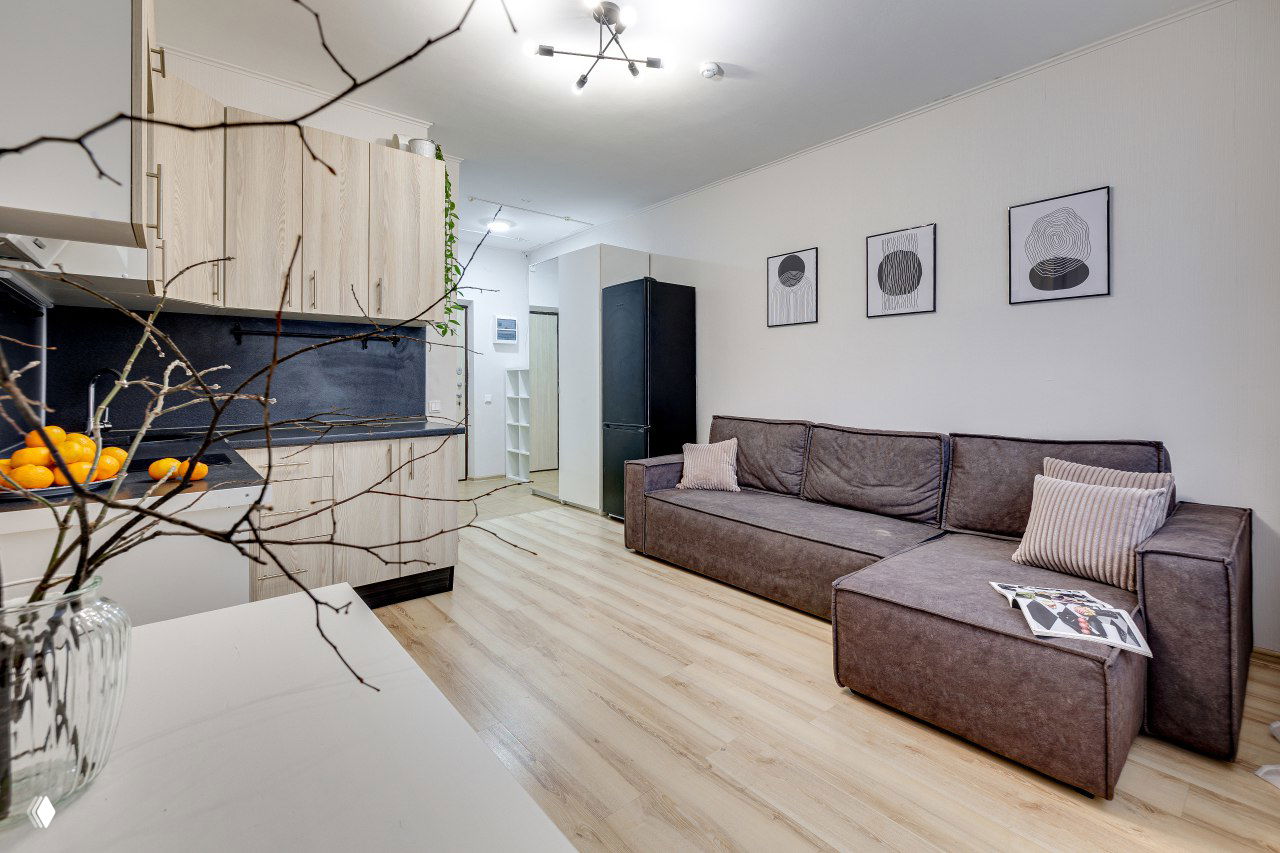 Гостиная-кухня в светлых тонах после предпродажной подготовки: диван, кухня, деревянный пол и декор, демонстрирующие уют и визуальную целостность помещения.