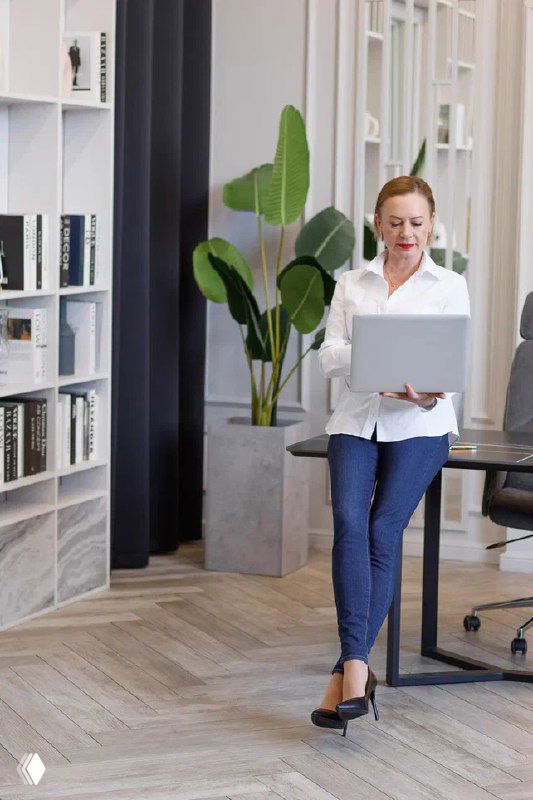 Женщина-агент по недвижимости с ноутбуком в современном офисе — книжные полки, горшечное растение и рабочее место на фоне.