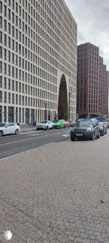 Современные фасады жилых кварталов ЗИЛАРТ с арочным проходом, улица и припаркованные машины на фоне урбанистического пространства.