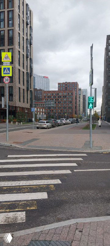 Перекрёсток и тротуар у жилого комплекса ЗИЛАРТ, дорожные знаки, пешеходный переход и городской пейзаж в пасмурный день.