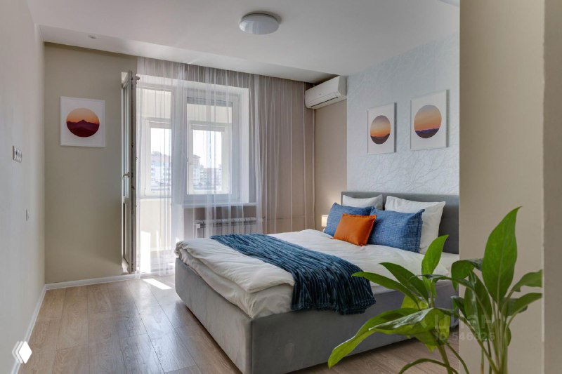 Светлая спальня с выходом на балкон, оформленная под целевую аудиторию: постельные тона, декоративные подушки и зелёный акцент.