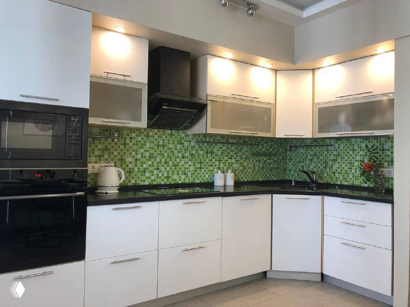 Современная кухня с белыми фасадами и плиточной фартукой, показанная под выгодным углом для объявлений о продаже недвижимости.