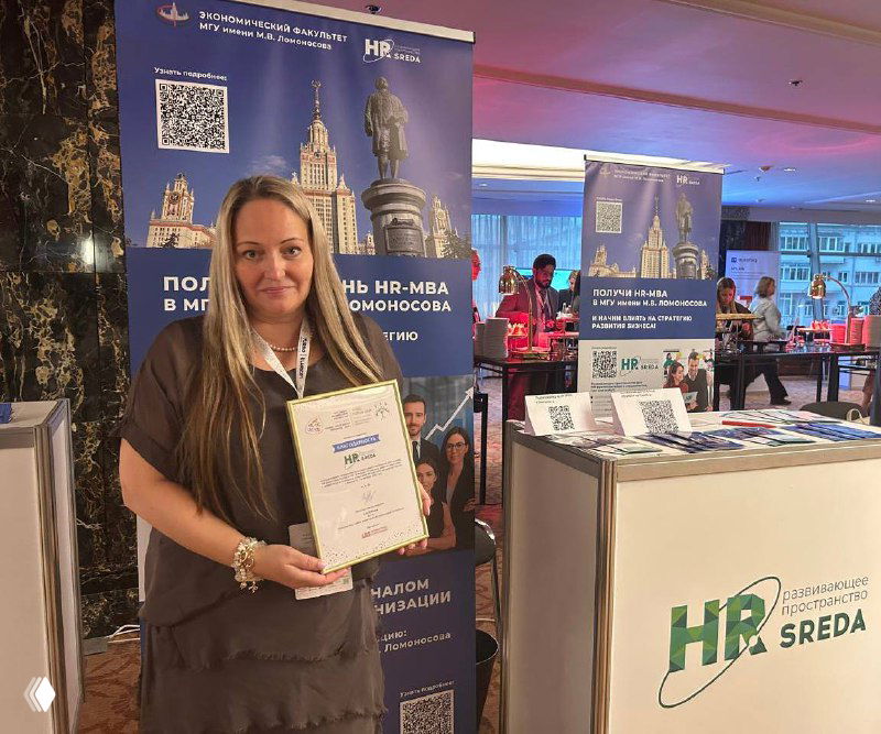 Участница у промо‑стола HR‑SREDA держит сертификат на фоне баннера с информацией о совместных обучающих программах и логотипом клуба.