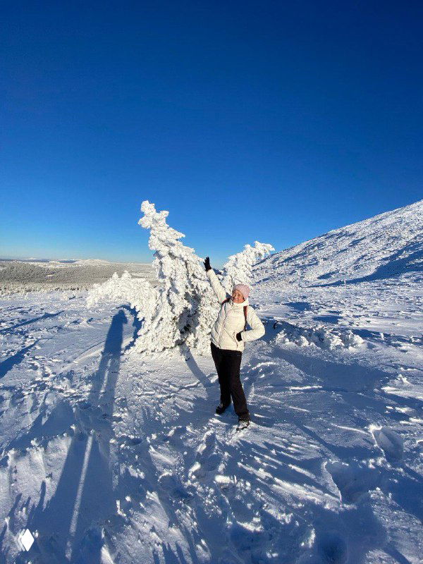 Туристка на фоне заснеженного склона и голубого неба: человек в яркой одежде на снежном фоне для фотосессии в походе.