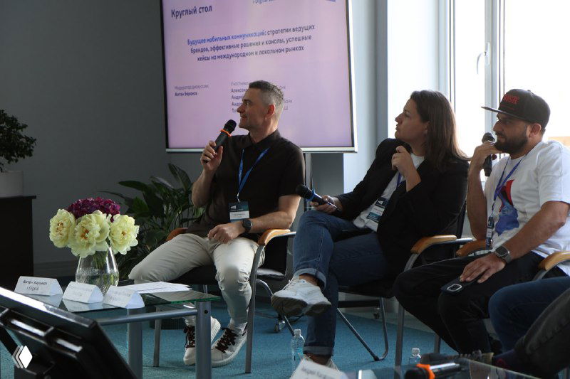 Круглый стол с экспертами: модераторы и участники с микрофонами в деловой зоне, заметна атмосфера живого обсуждения.
