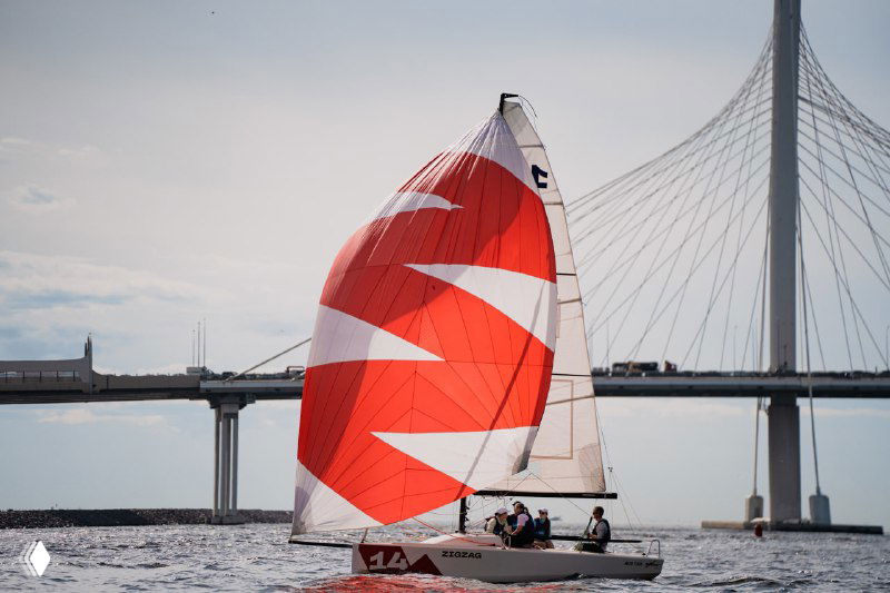 Парусная регата на фоне современной архитектуры и моста в Санкт-Петербурге; яхта с красным спинакером на воде.