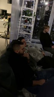 Группа людей на встрече: несколько человек сидят у окна, на фоне декоративная лестница с огоньками и напитками.