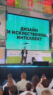 Выступление на сцене Startup Village: докладчик на фоне большого экрана с текстом о дизайне и искусственном интеллекте, зрители на переднем плане.