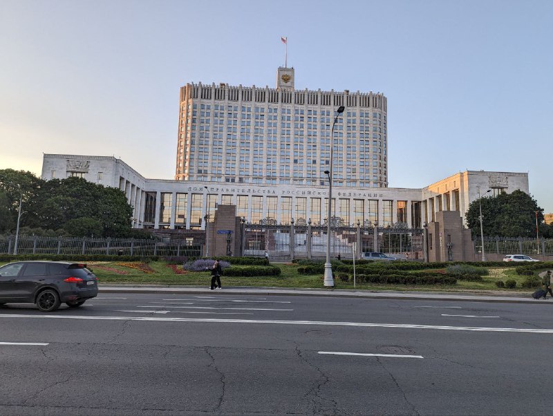 Широкий городской проспект с многоэтажным зданием во фронтальной части и полосой движения; вечернее или утреннее освещение на фасадах.