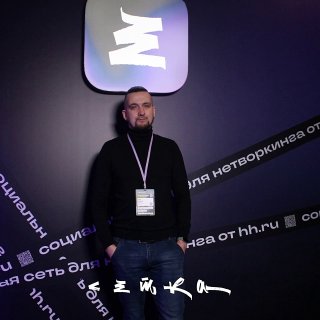 Портрет мужчины на фоне бренд‑волла для нетворкинга, у него бейдж на шее, кадр сделан в деловой, но неформальной обстановке.