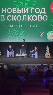 Сцена и аудитория на новогоднем мероприятии в Сколково: выступающие на сцене, декорации с надписью и расположение зрительных рядов в зале