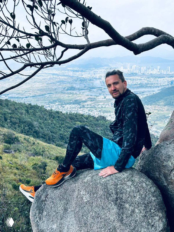 Автор отдыхает на большом камне с видом на город и побережье внизу, кадр демонстрирует сочетание природы и городской панорамы за спиной.