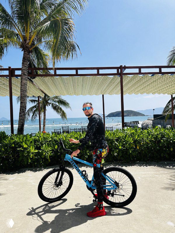 Человек на велосипеде на фоне пальм и панорамы набережной, кадр символизирует мобильность и жизнь у моря во время проживания в Нячанге.