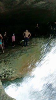 Водопад в скальной нише с сильными брызгами на переднем плане; несколько людей стоят у воды, видно место для ныряния
