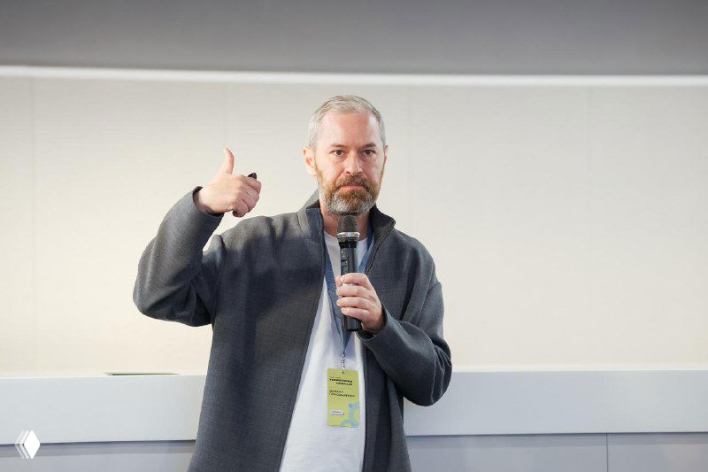 Лектор с бейджем держит микрофон и показывает палец вверх во время выступления на встрече со студентами, живое общение и лекция.