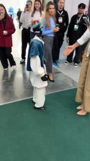 Небольшой человекоподобный робот‑аниматор на выставке в окружении публики: дети и взрослые наблюдают за развлечением в павильоне