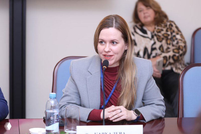 Татьяна Кархалёва выступает за столом круглой дискуссии, микрофон, бутылка воды и документы на столе, кадр во время обсуждения вопросов ИС в моде.