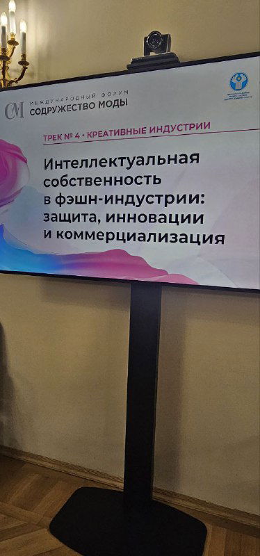 Информационный стенд с афишей круглого стола «Интеллектуальная собственность в фэшн-индустрии: защита, инновации и коммерциализация», установленный в зале мероприятия.